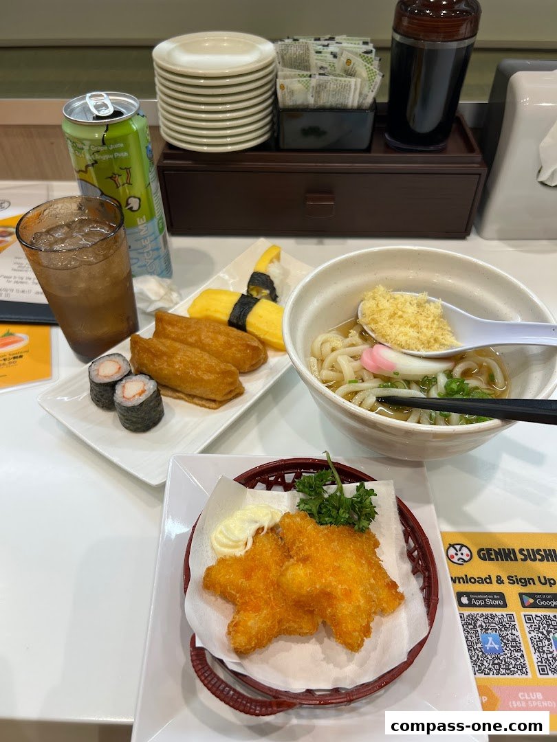 A table at Genki Sushi with various sushi, udon, and fried items, plus drinks.
