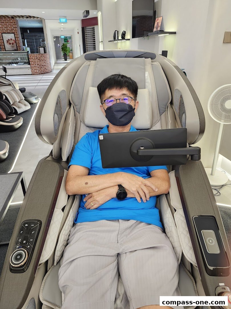 A man sits in a massage chair with a tablet attached, in a well-lit retail store.