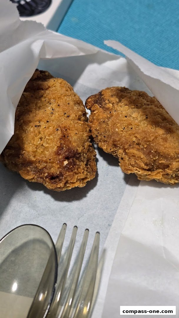Two pieces of golden-brown fried chicken are presented in white paper with a fork and spoon.