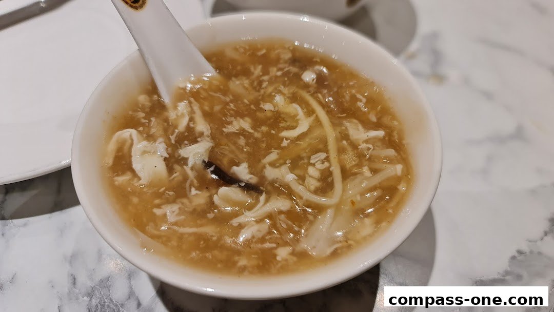 A close-up shot of a bowl of hot and sour soup with shredded chicken and mushrooms.