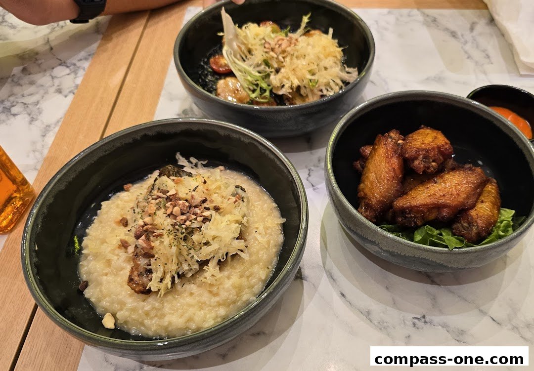 Three bowls of food, including risotto, chicken wings, and a salad, are arranged on a marble table.