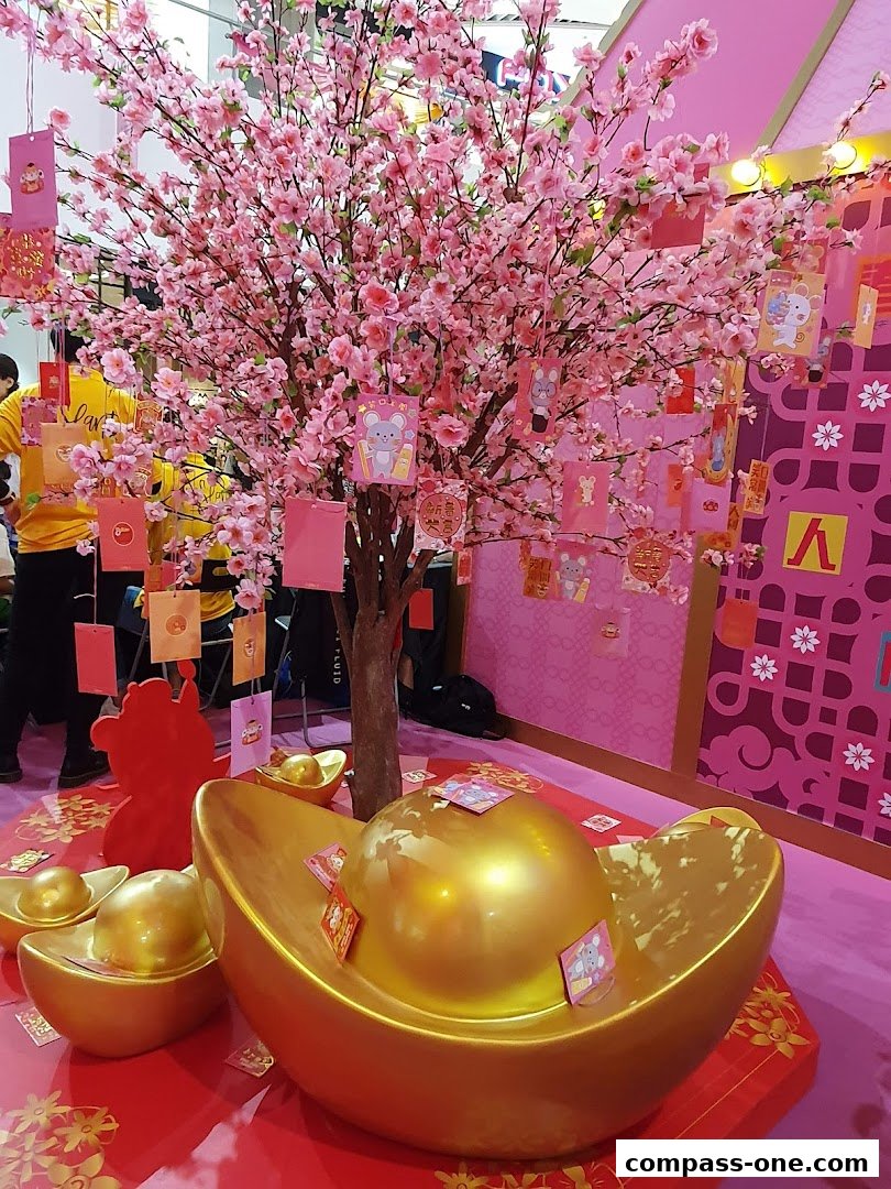 A festive display with a blooming cherry blossom tree adorned with red and pink ornaments and gold ingots.