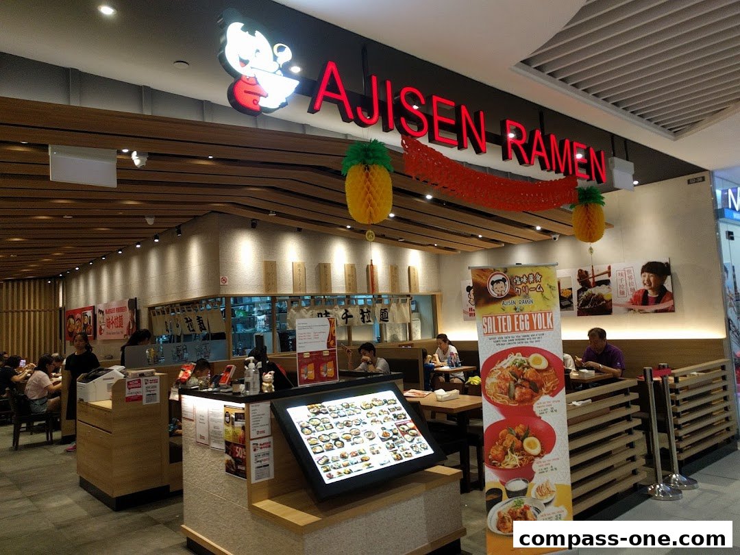 Interior view of Ajisen Ramen restaurant with customers dining and a digital menu display.