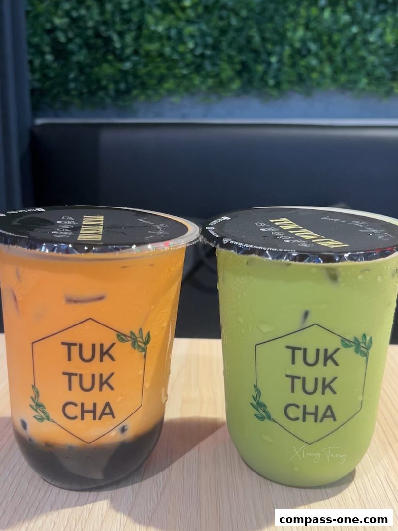Two refreshing bubble tea drinks, one Thai milk tea and one matcha, displayed on a wooden surface.