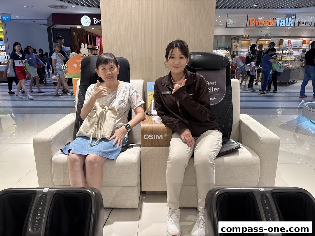 A woman and a staff member sit in OSIM massage chairs, with a BreadTalk store in the background.