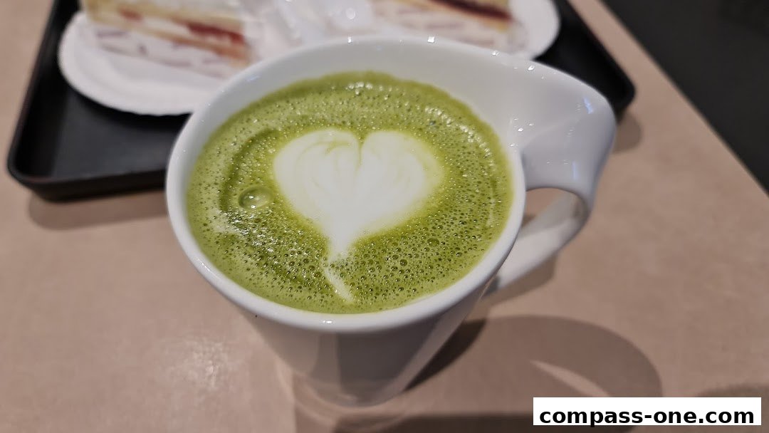 A close-up of a matcha latte with a heart-shaped foam art in a white mug.