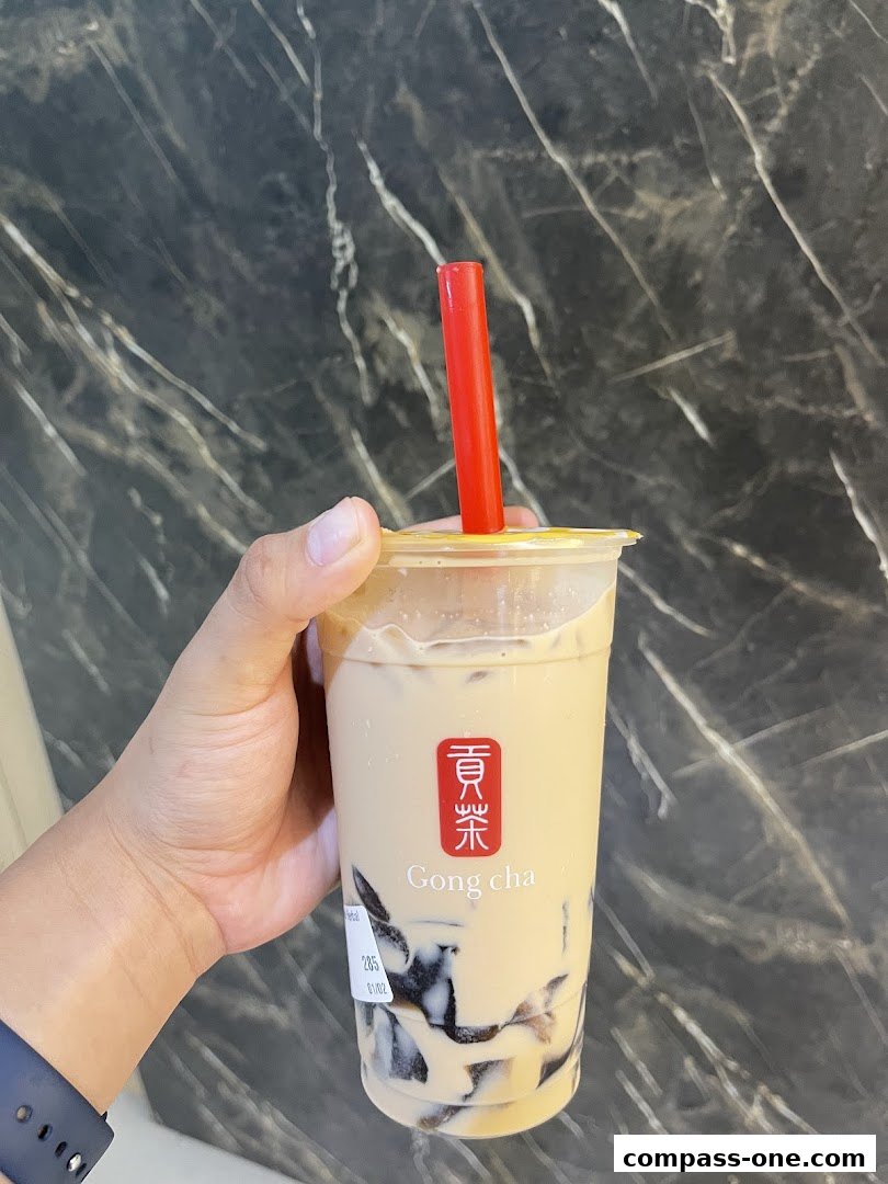 A hand holds a Gong Cha bubble tea with grass jelly and a red straw.
