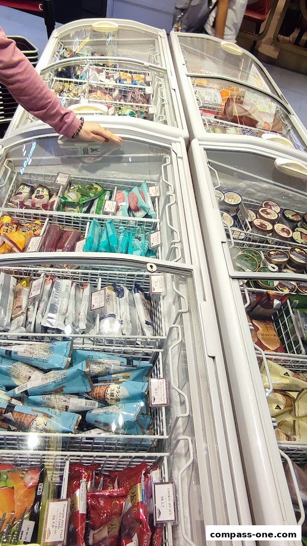 A person's hand opens a freezer door revealing rows of packaged ice cream and frozen desserts.