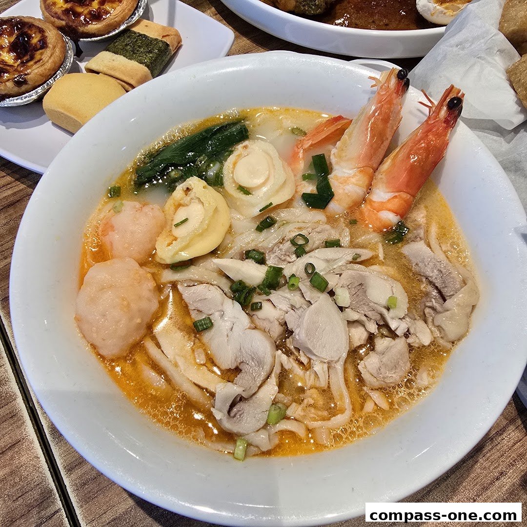 A close-up of a steaming bowl of Ipoh hor fun with chicken, shrimp, and fish balls.