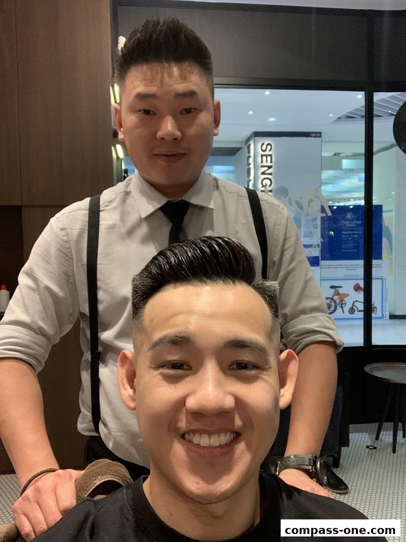 A barber stands behind a smiling customer, both showing off stylish haircuts.