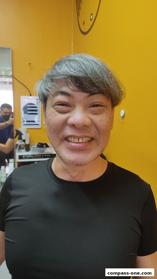 A smiling man with grey hair poses in a brightly lit salon with yellow walls.