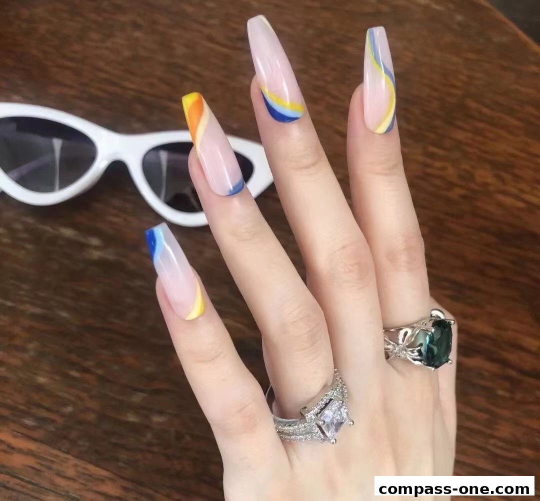 A hand with long, colorful French tip nails and rings, next to white sunglasses.