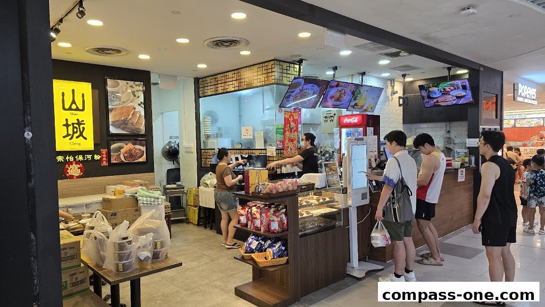 Customers ordering at a counter with food displays and digital menus inside a shop.
