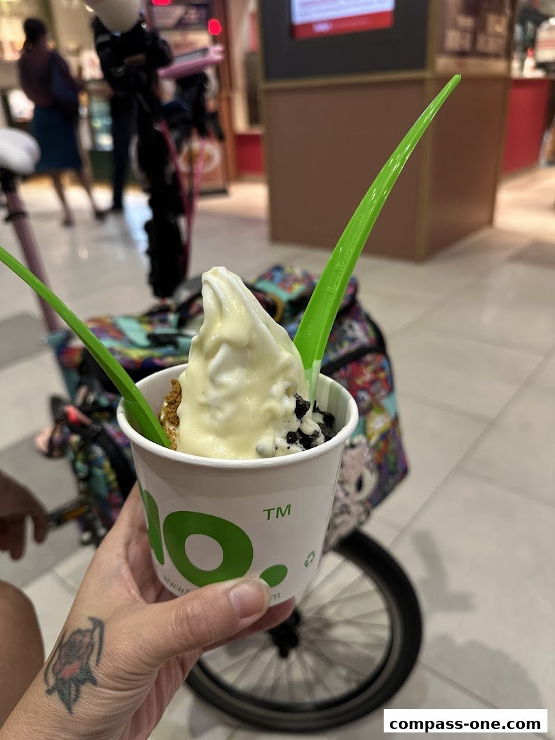 A hand holds a cup of frozen yogurt with toppings and green spoons.
