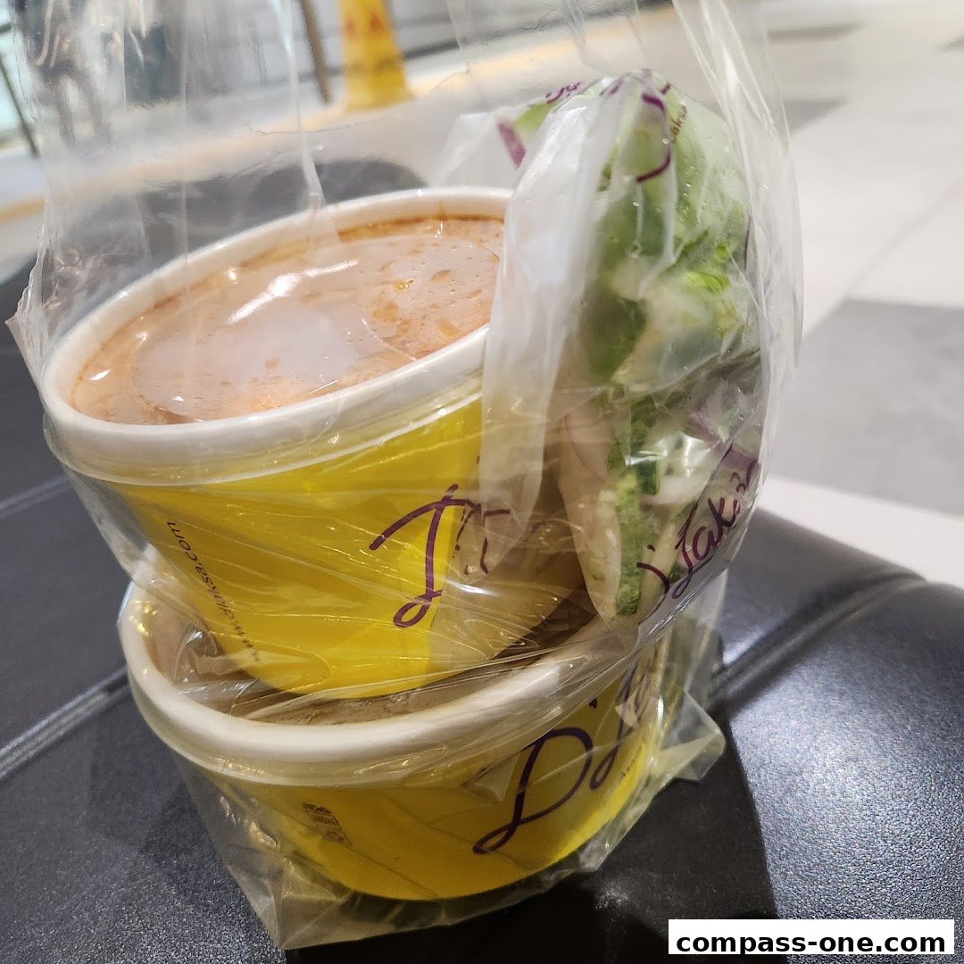 Two yellow takeaway containers with food, one with soup and the other with salad, in a plastic bag.