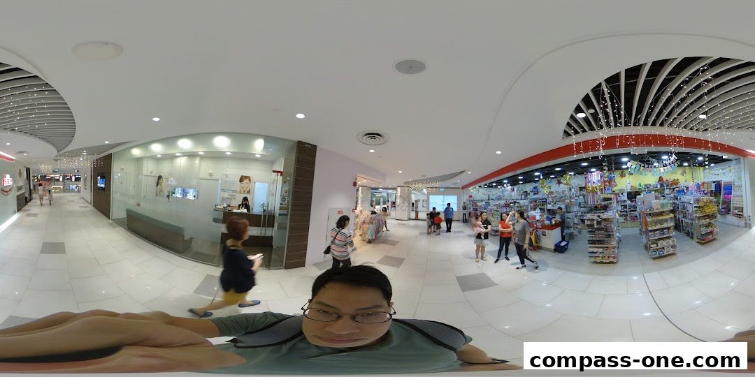 A wide-angle view of a shopping mall corridor with various shops and people.