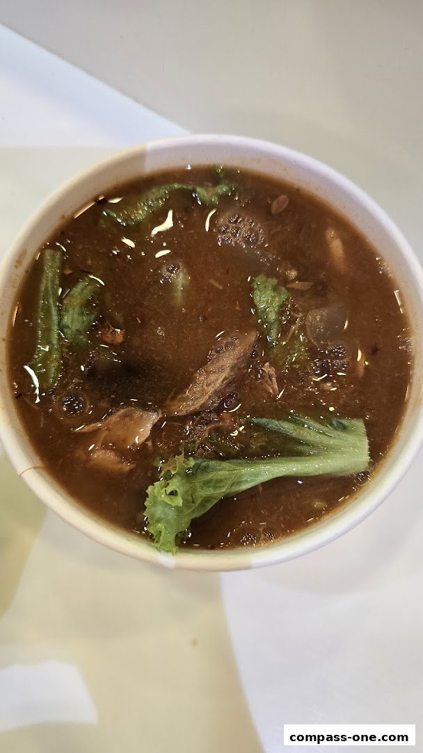 A close-up shot of a bowl of Laksa with visible noodles, meat, and vegetables.