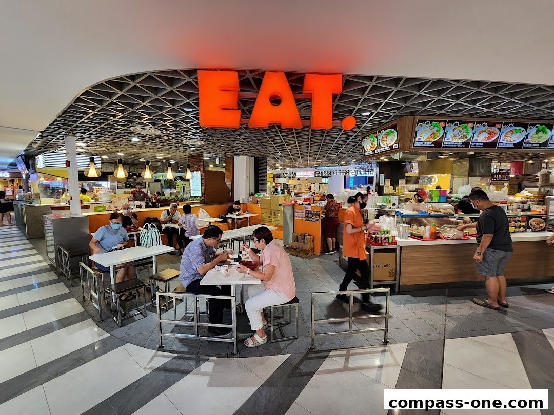 People dining at tables in a food court with a large 'EAT.' sign.