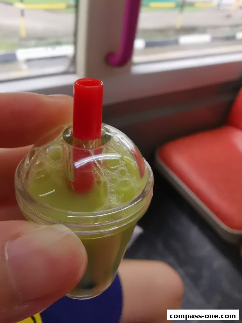 A hand holds a miniature bubble tea cup with green liquid and a red straw.
