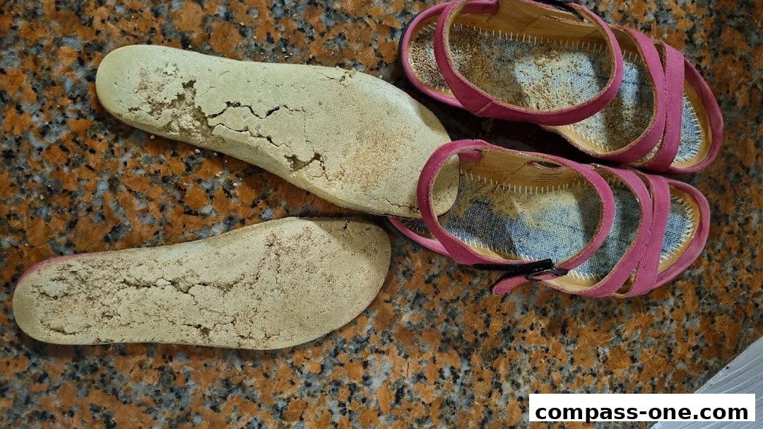 Close-up of worn-out insoles and pink sandals on a speckled surface.