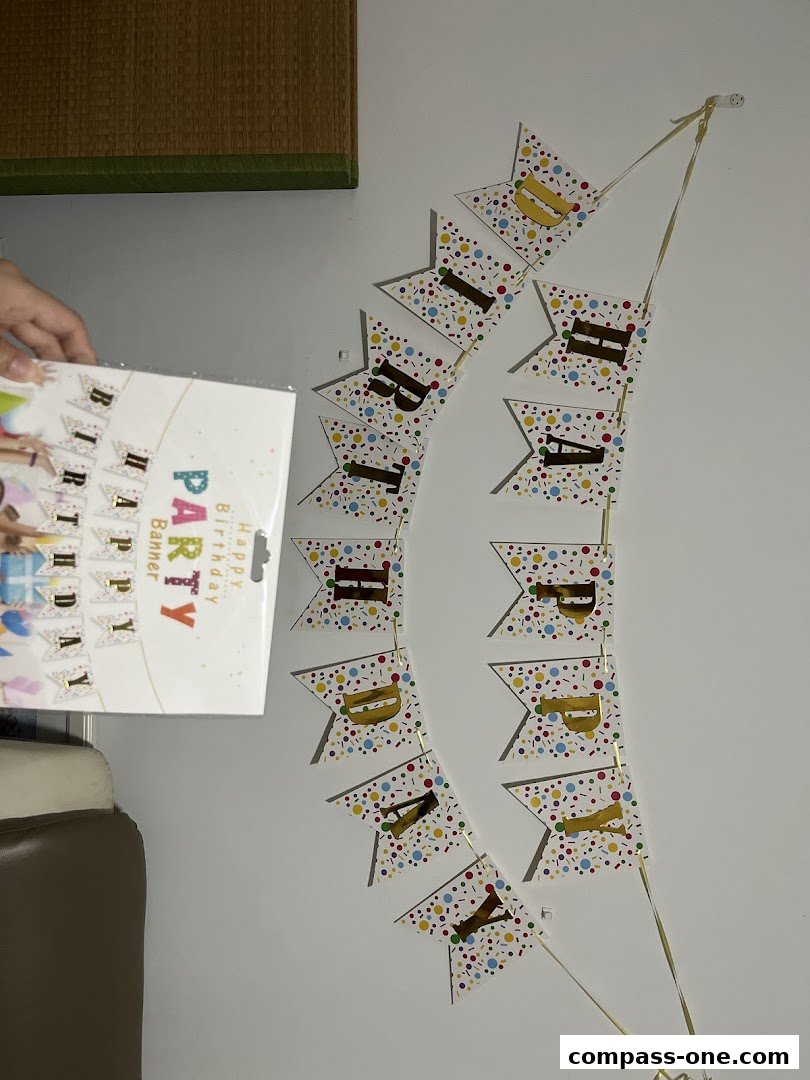 A birthday banner with colorful confetti pattern and gold lettering hangs on a wall.