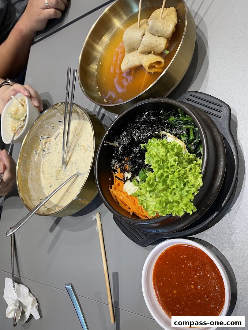 A table laden with Korean street food dishes, including fish cakes, bibimbap, and dipping sauce.