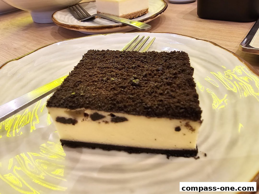 A slice of cheesecake with a dark crumb topping and cookie pieces on a decorative plate.