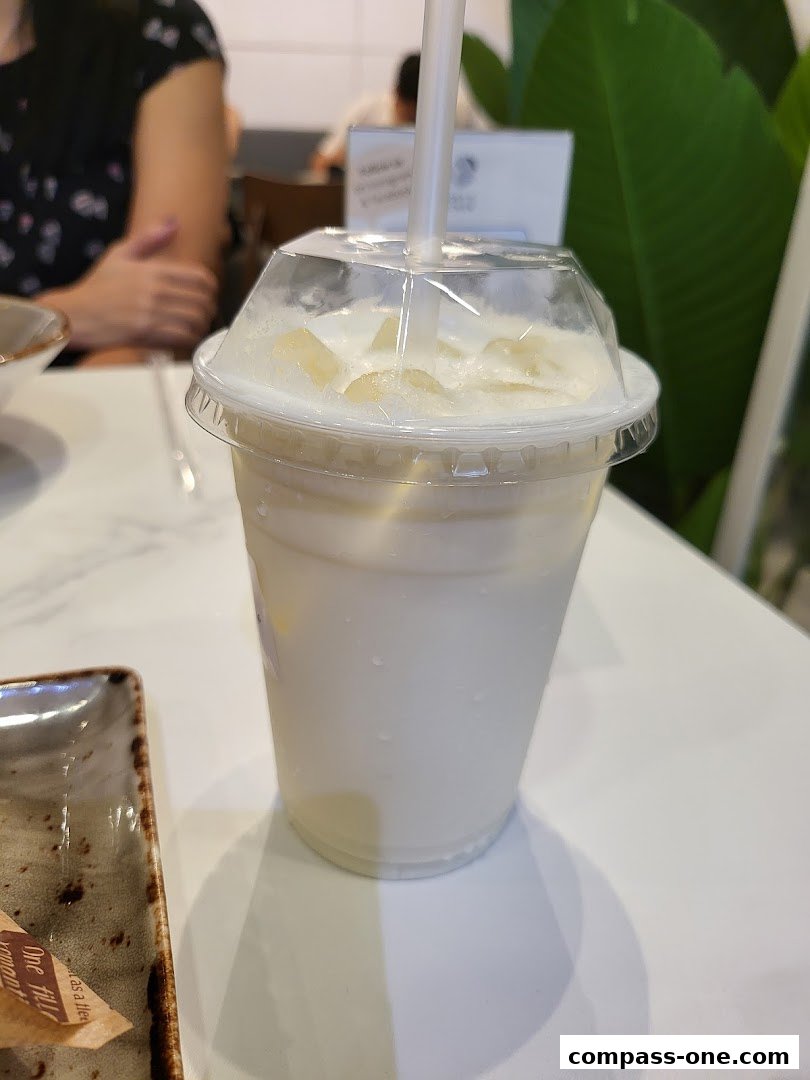 A close-up of a creamy beverage with ice and a straw in a clear plastic cup.