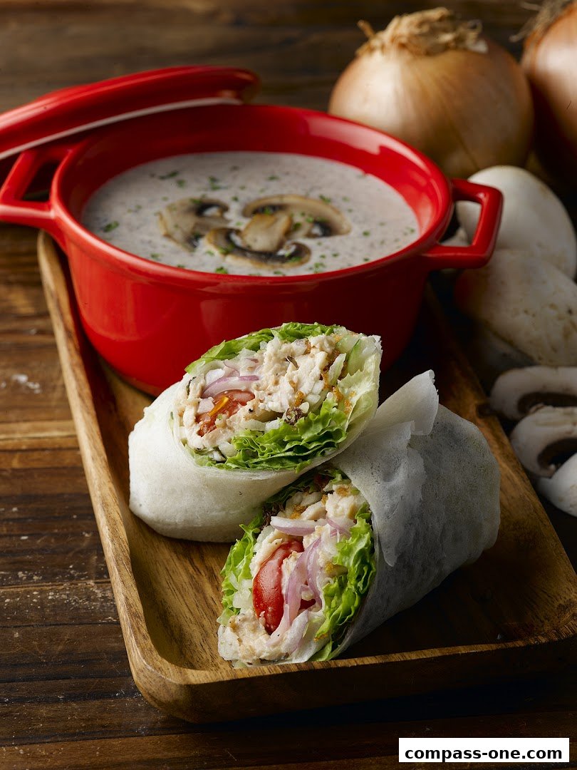 A delicious chicken wrap and creamy mushroom soup served on a wooden tray.