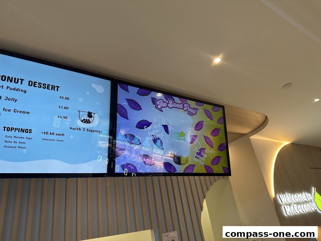 A digital menu board displaying coconut desserts and toppings with prices.