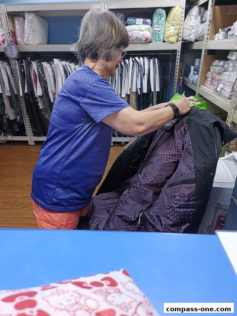 A woman is organizing clothes on hangers in a dry cleaning and laundry service shop.