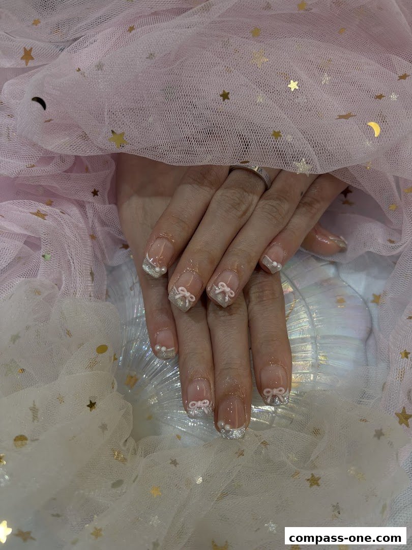 Close-up of hands with French manicured nails adorned with bows and pearls.