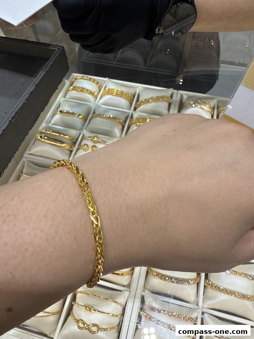 A hand wearing a gold bracelet with various gold jewelry displayed in the background.