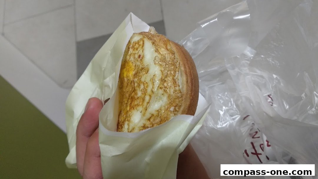 A hand holds a freshly made egg sandwich wrapped in paper and plastic.