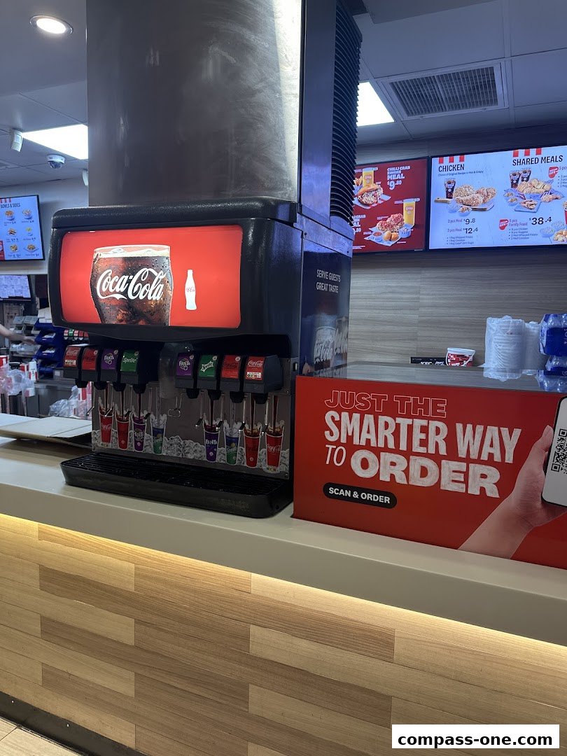 KFC counter with a Coca-Cola dispenser and digital menus displaying chicken meals.