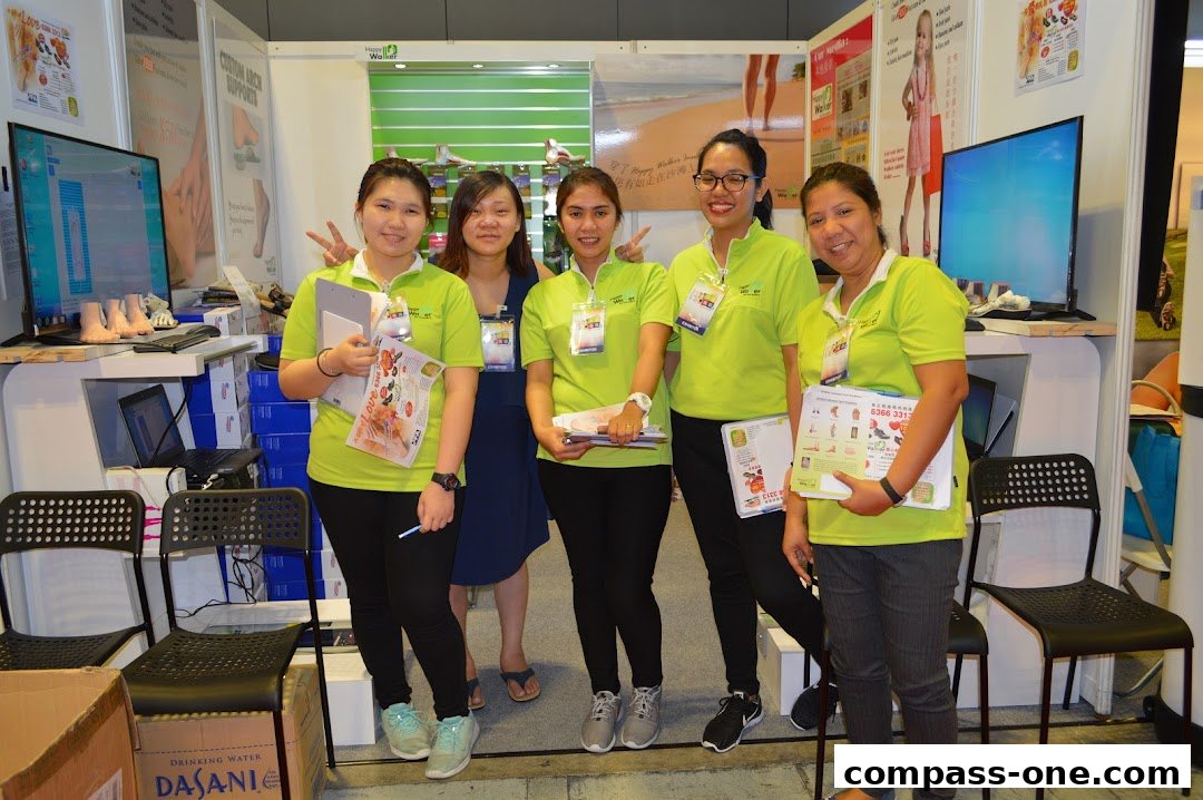 A group of five women in bright green shirts stand at a retail booth, holding promotional materials.