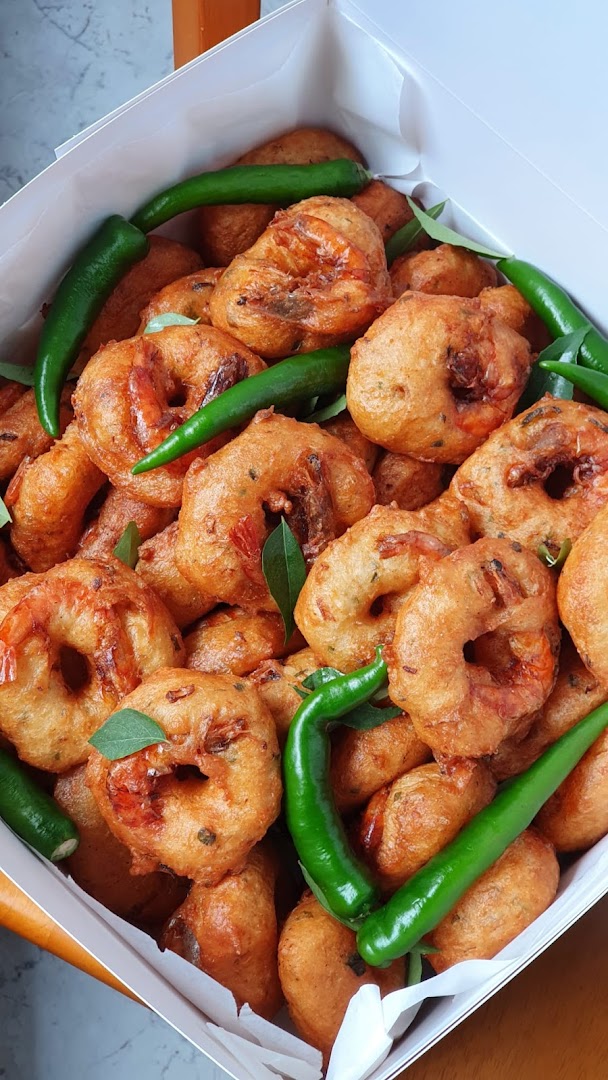 A box filled with golden-brown shrimp fritters (vada) garnished with green chilies and curry leaves.
