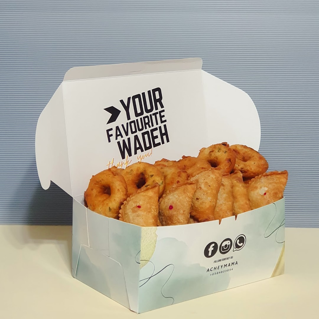 A white box filled with golden-brown fried snacks, including vadeh and curry puffs.