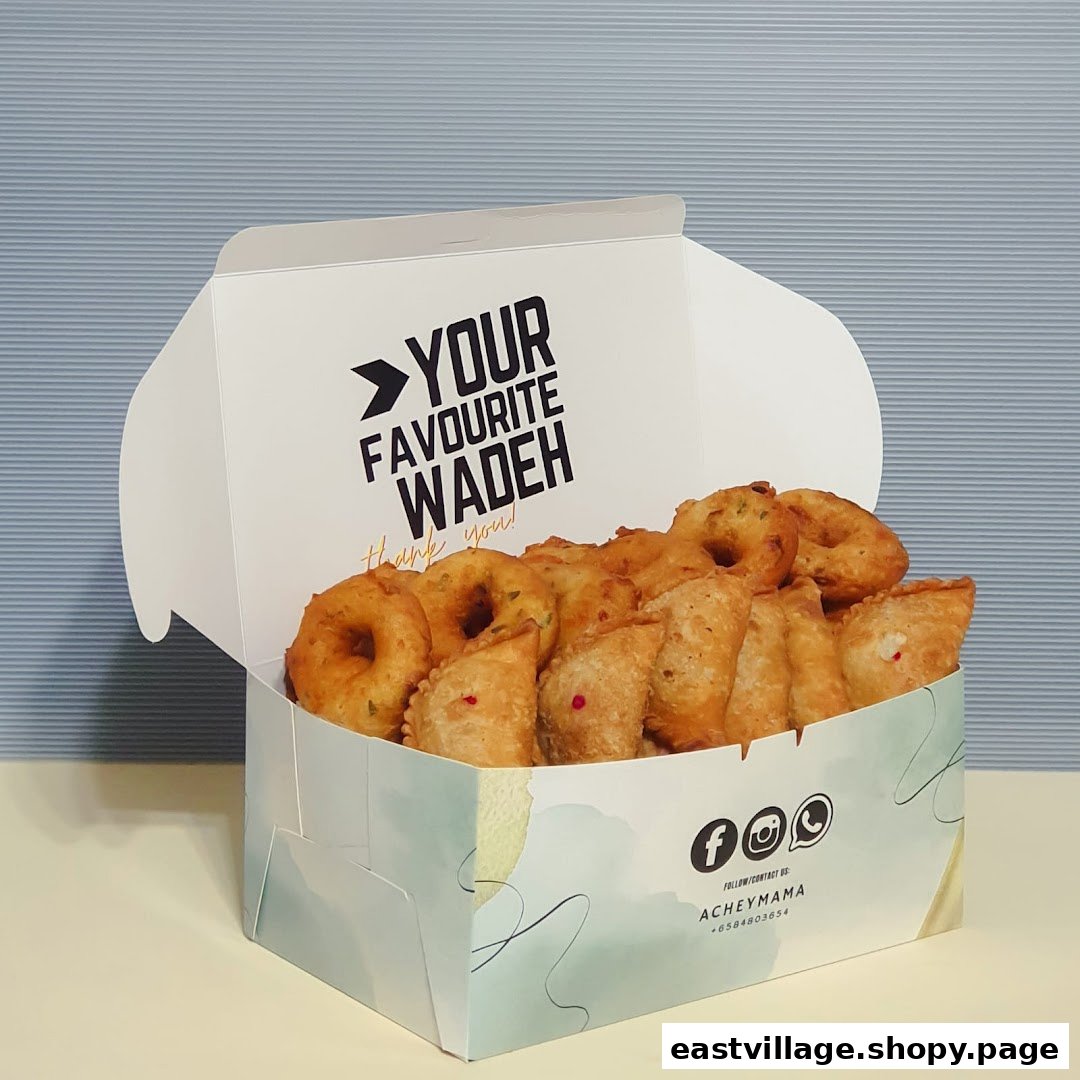 A white box filled with golden-brown fried snacks, including vadeh and curry puffs.