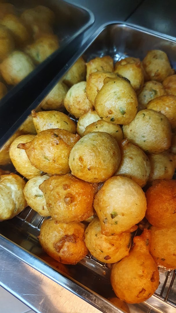 A close-up of golden-brown, fried fritters or savory snacks, displayed in a metal serving tray.