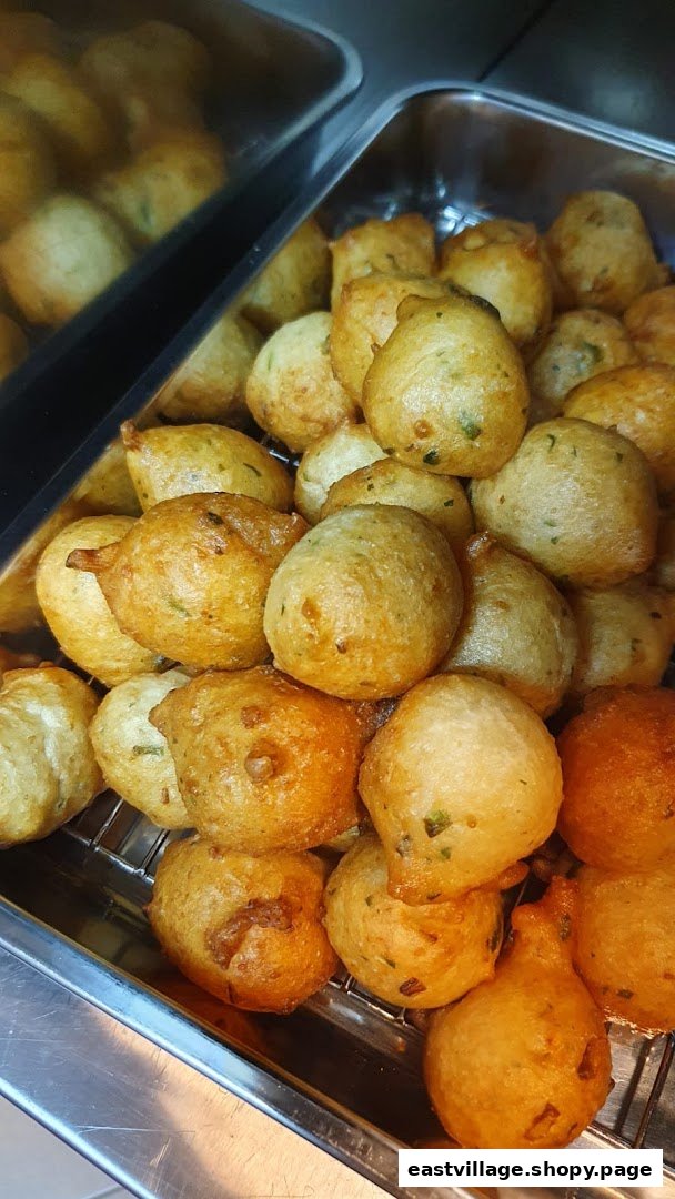 A close-up of golden-brown, fried fritters or savory snacks, displayed in a metal serving tray.