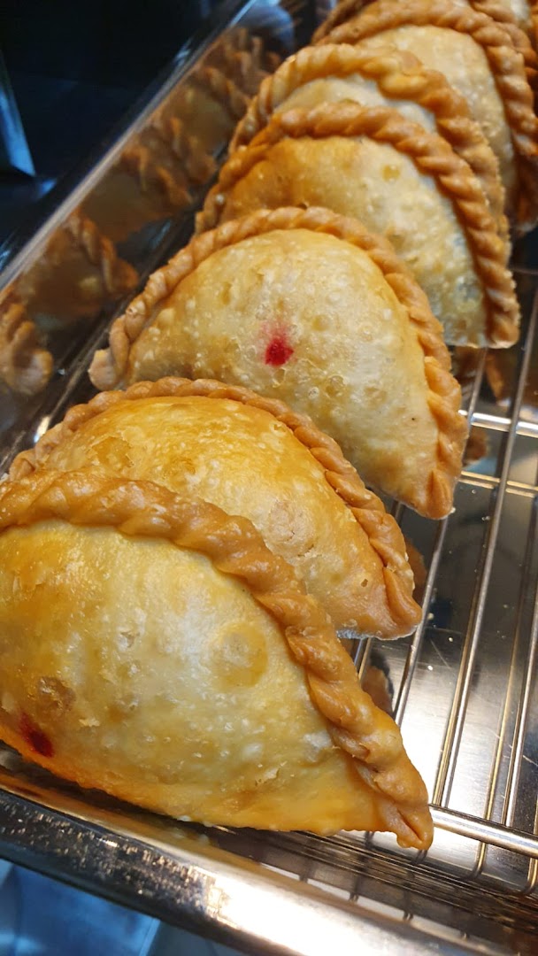 A close-up of several golden-brown, crimped pastries, possibly curry puffs, displayed on a metal rack.