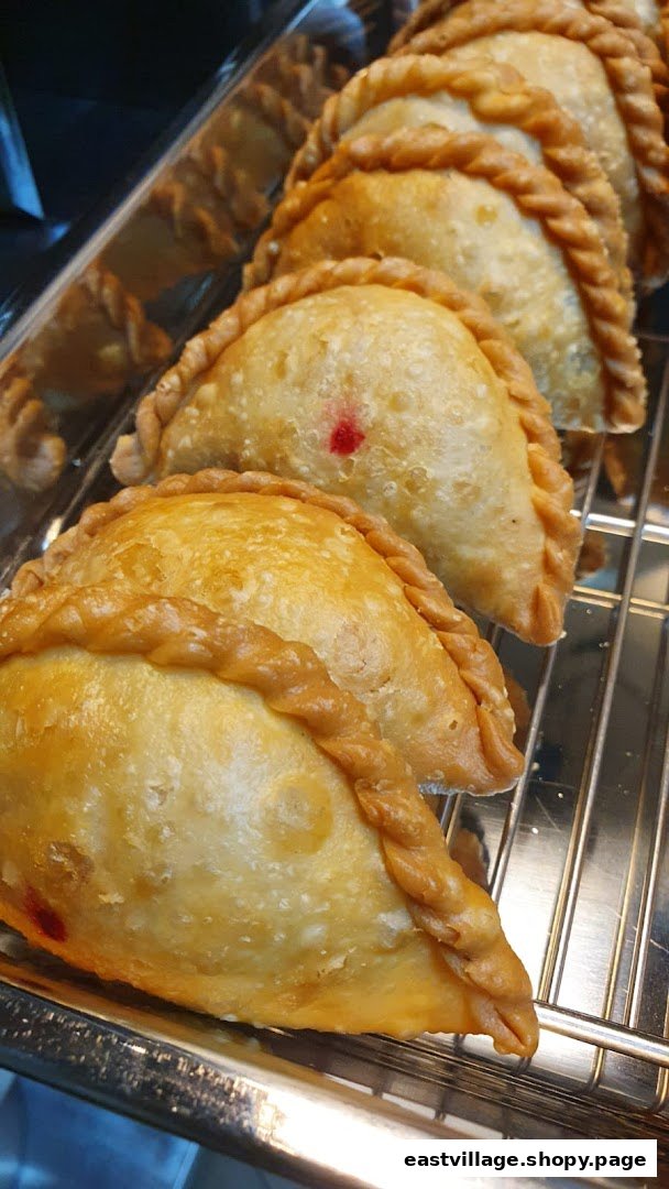 A close-up of several golden-brown, crimped pastries, possibly curry puffs, displayed on a metal rack.