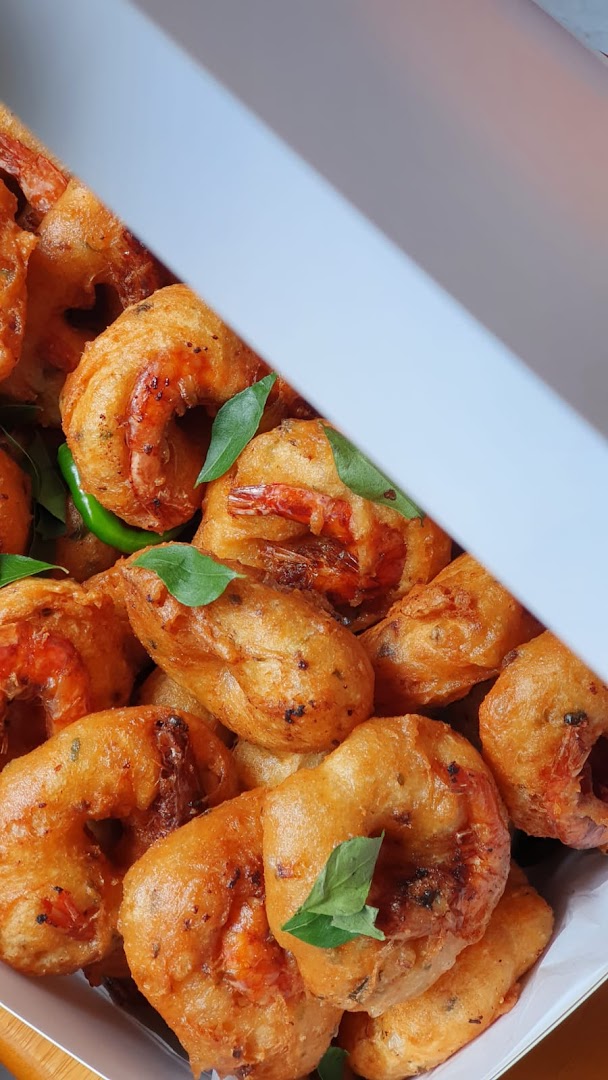 Golden-fried shrimp fritters or vada, garnished with fresh curry leaves and green chilies in a box.