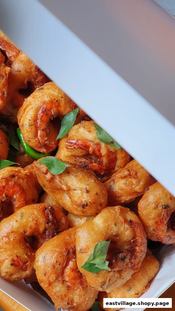 Golden-fried shrimp fritters or vada, garnished with fresh curry leaves and green chilies in a box.