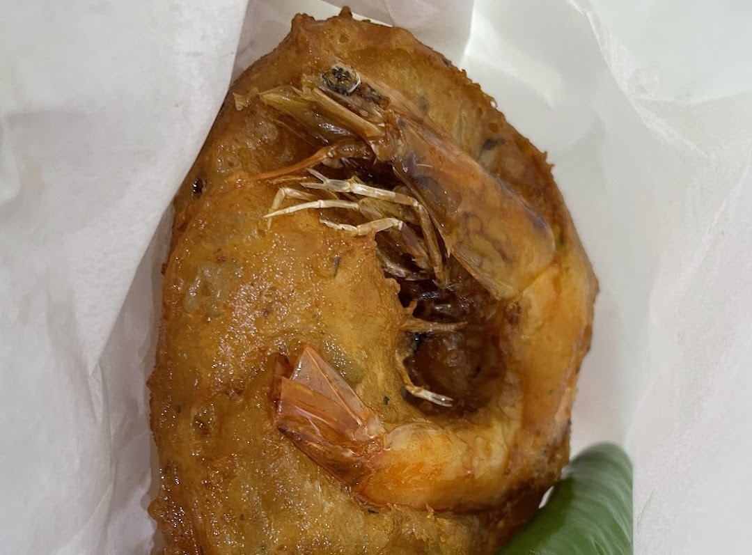 A golden-brown deep-fried fritter with a whole shrimp, wrapped in white paper.
