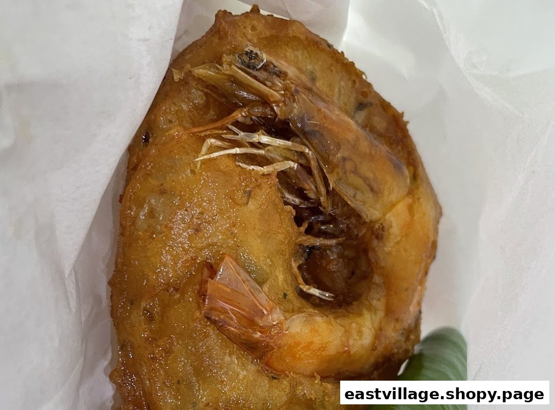 A golden-brown deep-fried fritter with a whole shrimp, wrapped in white paper.