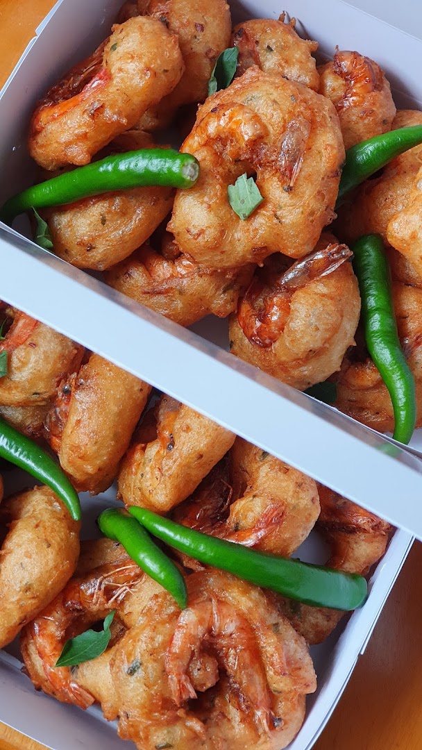 Golden-fried shrimp fritters with green chilies and curry leaves in a white box.