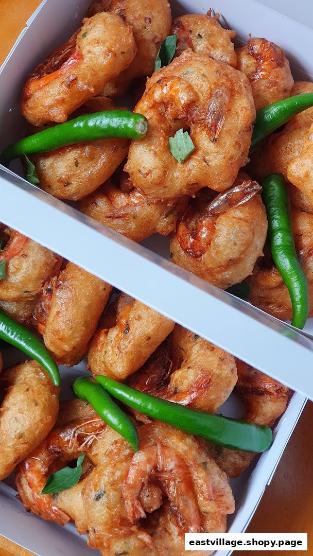 Golden-fried shrimp fritters with green chilies and curry leaves in a white box.