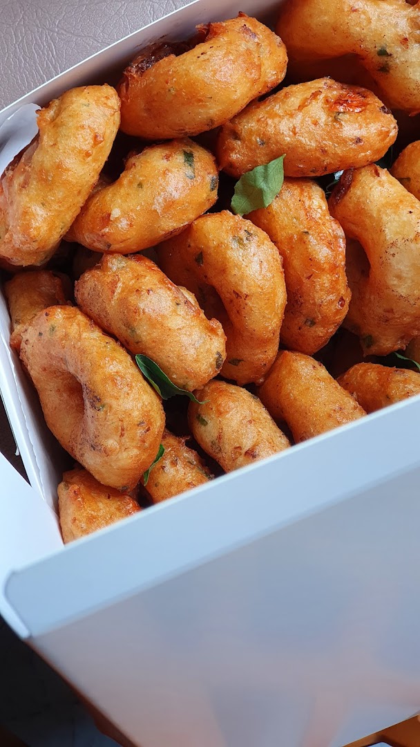 A white box filled with golden-brown, savory fried snacks, some garnished with green leaves.